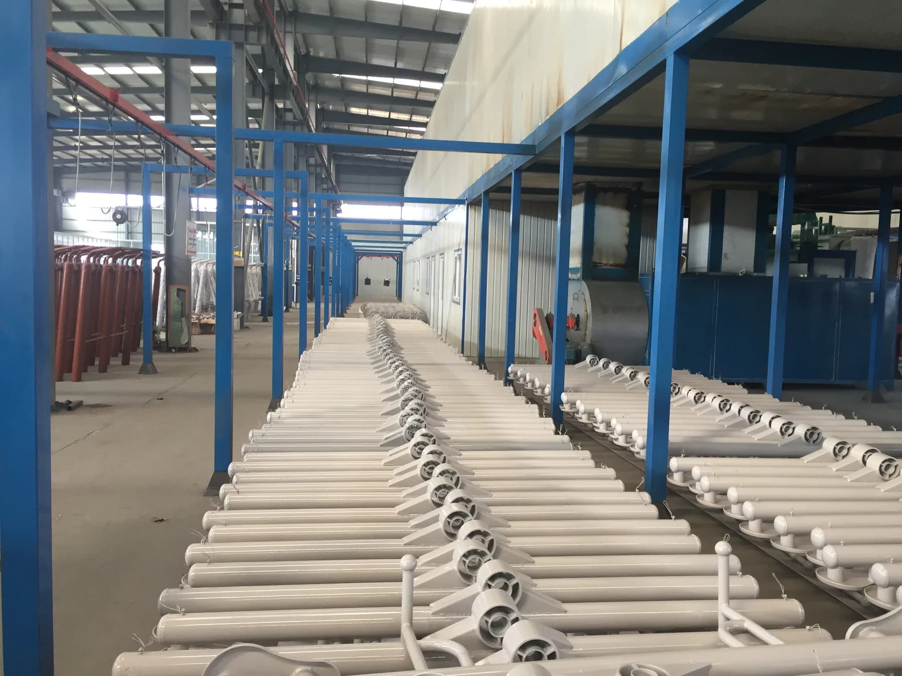 Rows of prepared white steel components beside workshop coating equipment